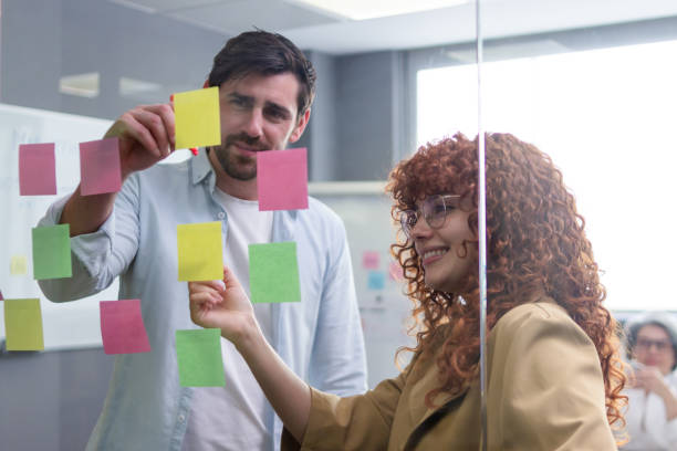 istock Creative colleagues brainstorming with sticky notes on glass wall in coworking space 2187995126