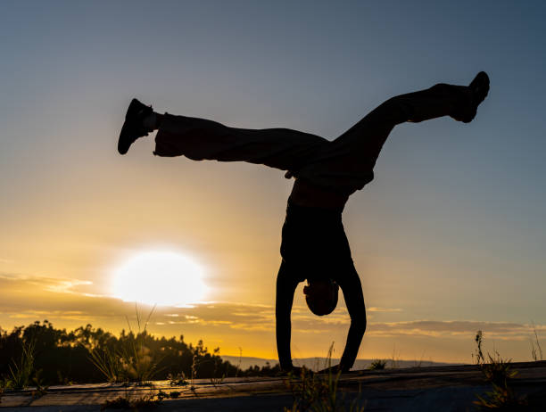 Backlit silhouette of a woman doing a face-down breakdance pirouette at sunset. The sunset, with the sky as a backdrop, adds a warm scene