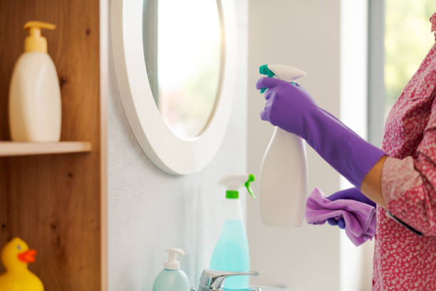 Woman cleaning the bathroom at home, she is polishing the mirror using a spray detergent