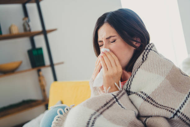istock Charming brunette sneezing in living room while wrapped in a cozy plaid blanket 2187996457