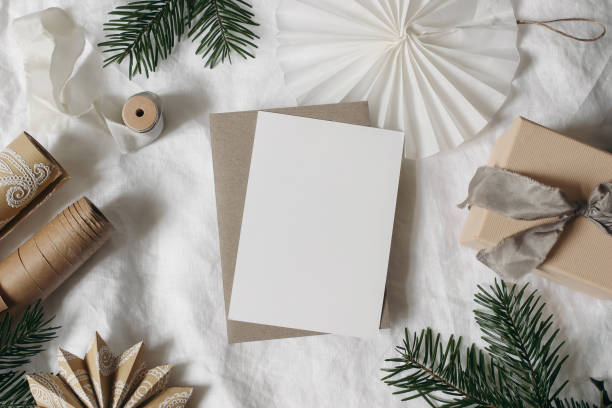 istock Christmas still life. Blank greeting card invitation mockup. Fir tree branches, gift box, wrapping paper. Paper star, rosette. White linen table cloth background. Winter flat lay, top view. 2187996648
