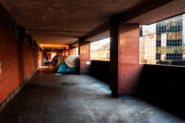Berlin, Germany – January 1, 2026: A makeshift shelter with a covered sleeping area, a trolley, and personal belongings stands beside a graffiti wall with posters at night.