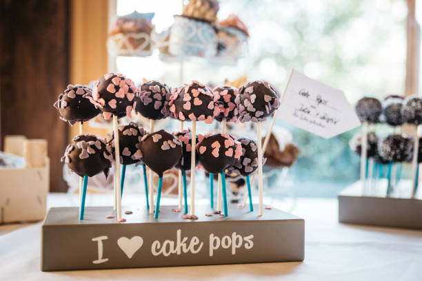 Delicious chocolate cake pops decorated with dark chocolate coating and pink heart-shaped sprinkles arranged on a wooden display stand with \
