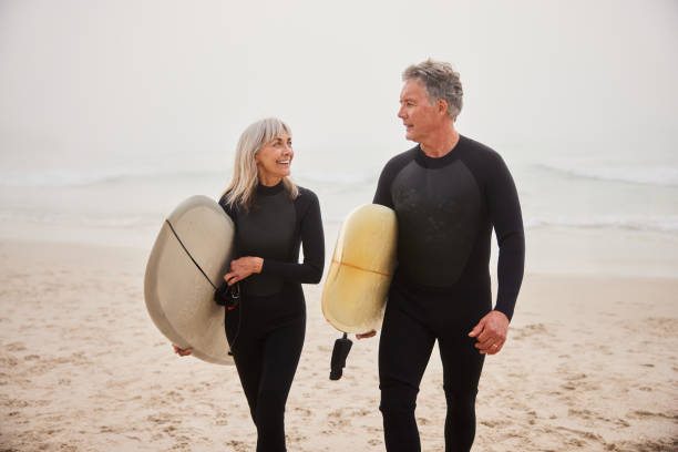 istock Senior couple holding surfboards on beach and talking 2187998315