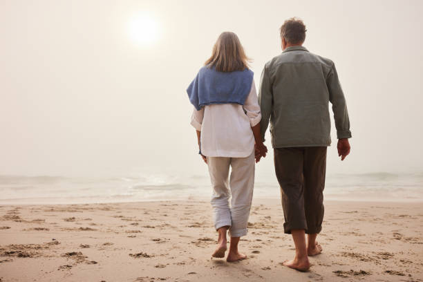 istock Senior couple having relaxing walk on beach, barefoot, rear view 2187998372