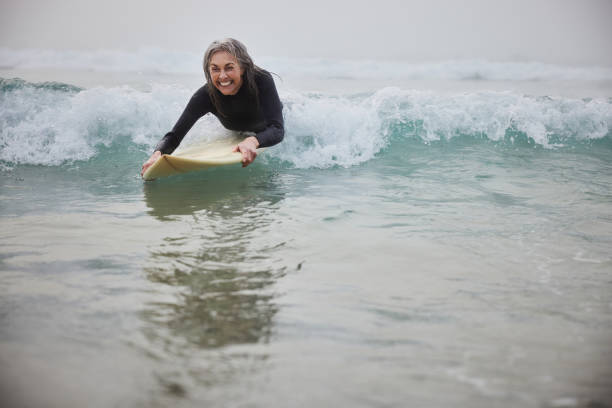 istock Senior woman lying on surfboard riding wave coming into shore 2187998428