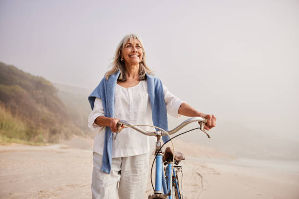 Active senior woman smiling and pushing bike on beach stock photo