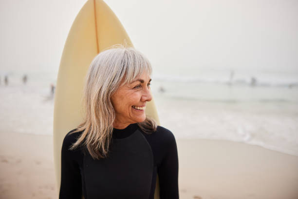 istock Senior female surfer with surfboard behind her back, smiling and looking away 2188002471