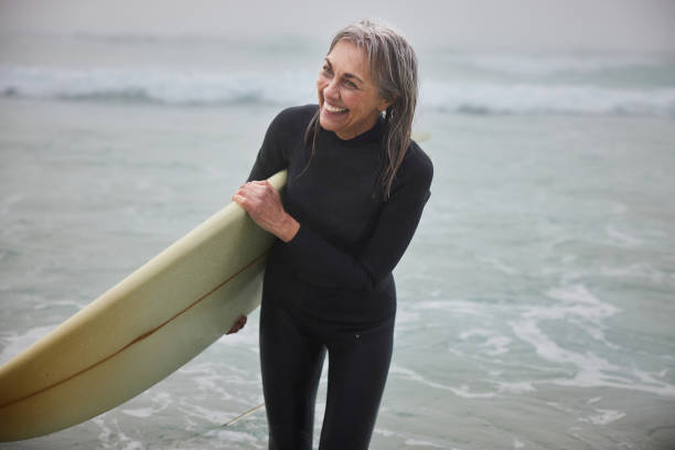 istock Senior female surfer carrying surfboard and laughing, looking away 2188002516