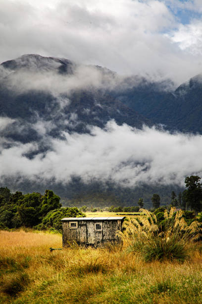 The raised hut on the shores of beautiful Ōkārito Lagoon, on the West Coast of New Zealand's South Island. In the distance we see the spectacular snowcapped peaks of the Southern Alps.