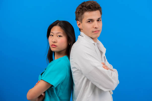 Confident doctor and nurse standing back-to-back with arms crossed, smiling on a vibrant blue background. The image highlights teamwork, professionalism, and positivity in healthcare.