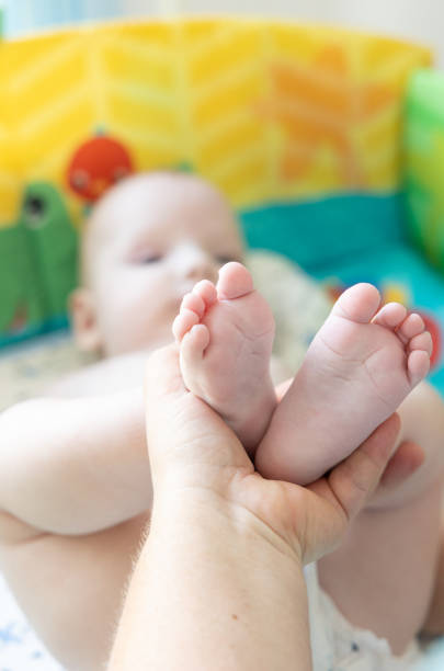 Close-up of a parent's hands gently holding a baby’s tiny feet against a colorful background. The image captures the warmth and tenderness of early childhood, showcasing a moment of love, care, and connection. Perfect for themes of family, parenthood, and nurturing.