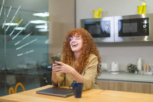 istock Young business woman laughing while using mobile phone in office break room 2188012112