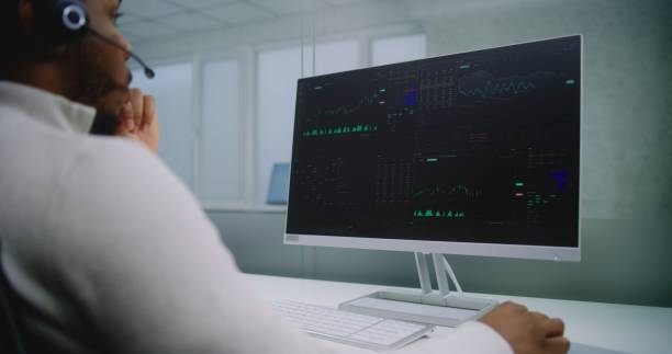 istock Stock exchange trader talks on headset, monitors equity market and shares using computer 2188013997