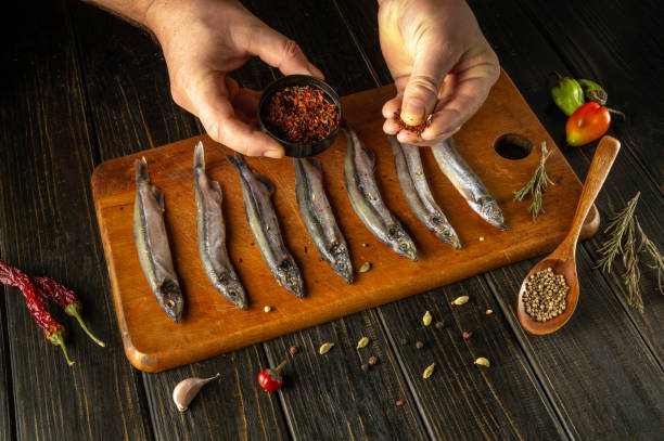istock Hands skillfully sprinkle spices over fresh fish laid on a wooden board. A warm, inviting kitchen ambiance showcases red chilies and herbs, perfect for creating a delicious meal. 2188015856