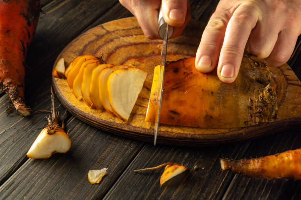 A chef skillfully cuts vibrant orange beetroot vegetables on a wooden cutting board. The warm kitchen ambiance enhances the focus on fresh ingredients for a delectable dish