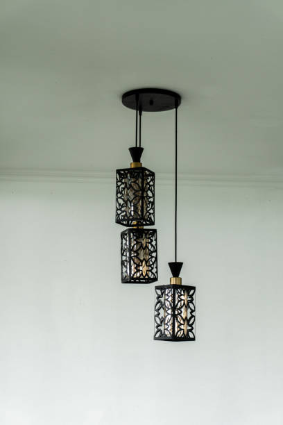istock three black pendant lights hanging from a light blue wall. The lights have intricate designs that resemble flowers and have a gold top. 2188019884