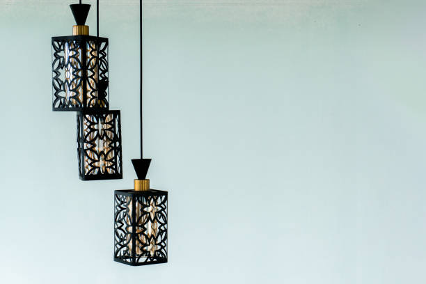 three black pendant lights hanging from a light blue wall. The lights have intricate designs that resemble flowers and have a gold top.