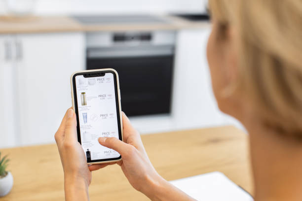 istock Caucasian woman browsing cosmetics on phone in modern kitchen 2188020586
