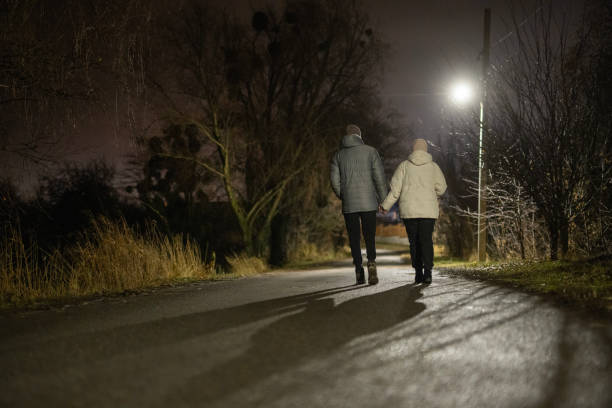 istock Couple holding hands while walking on a quiet road at night, illuminated by a streetlight, surrounded by bare trees and a serene atmosphere. 2188022372