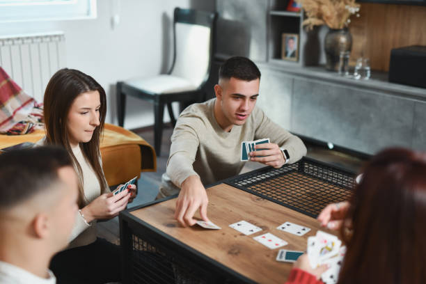 istock Handsome Male Picking up Cards from Table While Friends Are Waiting for His Next Move 2188023824
