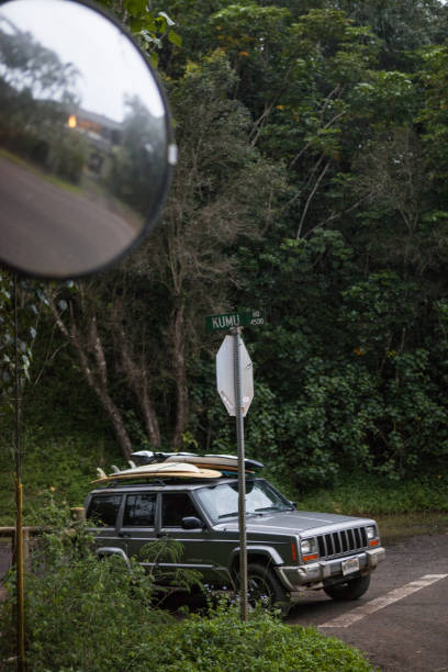 Shot of a road with a 4x4 and the dense hawaiian vegetation surrounding it, cloudy sky behind. Taken in Kauai, Hawaii, during the day.