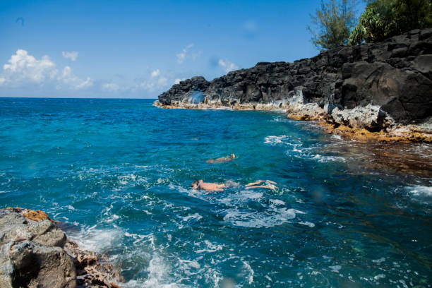Vast shot of a family snorkeling at an hidden volcanic rock beach. Taken in Kauai, Hawaii, during the day.