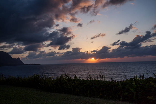 Vast shot of hanalei bay's view of a sunset falling on mountain and sea, cloudy sky above. Taken in Kauai, Hawaii, during the day.