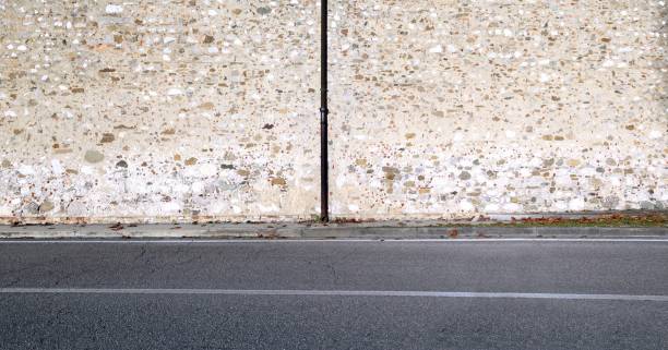 istock Gutter on old highconcrete and stone wall. Cement sidewalk and street in front 2188028099