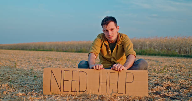 istock A man sits in a field holding a cardboard sign that reads Need Help. 2188029257