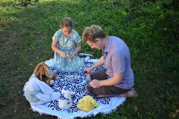 A little girl and her sister are sitting in the yard and using watercolors to paint pine cones.