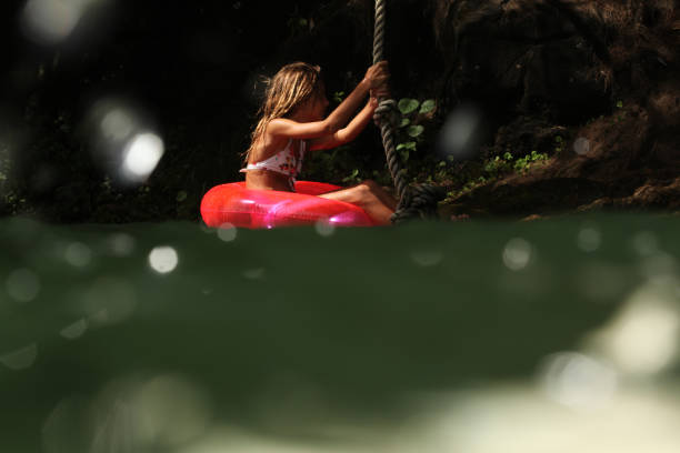 Shot of a girl floating on a river using a float, hanging onto a hanging rope, half underwater shot. Taken in Kauai, Hawaii, during the day.