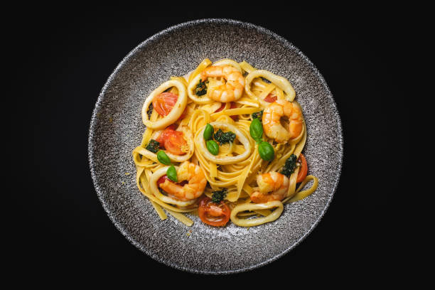 istock Appetizing pasta with herbs, vegetables and seafood on a black background. 2188034254