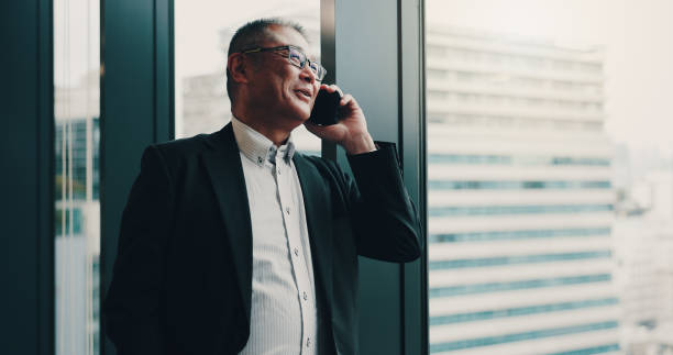 istock Japanese, businessman and office with phone call for communication, planning or networking by window. Thinking, male person and mature lawyer with mobile for talking, smile and case detail for client 2188038694