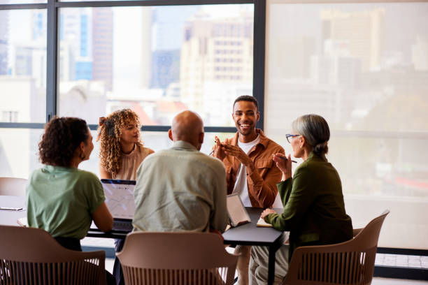 Cheerful mid adult man smiling and talking to four business colleagues in meeting stock photo