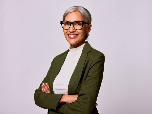 Portrait of mature woman with gray hair and glasses looking at camera, arms folded stock photo