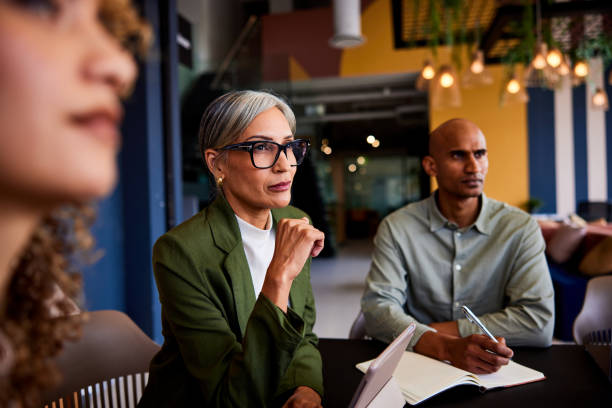 Confident female manager wearing glasses listening carefully in team meeting stock photo