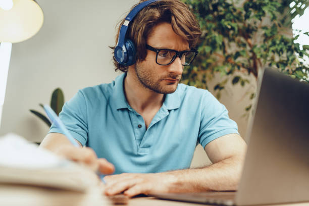 istock Young man in blue shirt sits at the table and studies with laptop 2188044082
