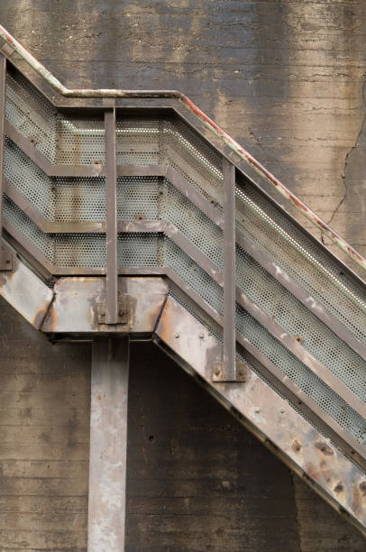 Rusty metal staircase with perforated steps fixed to a concrete wall, showing signs of age and wear