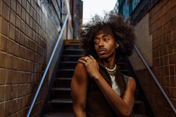 Confident young man with afro hair and wireless earphones poses on NYC subway stairs, exuding trendy urban style of generation z while lost in music