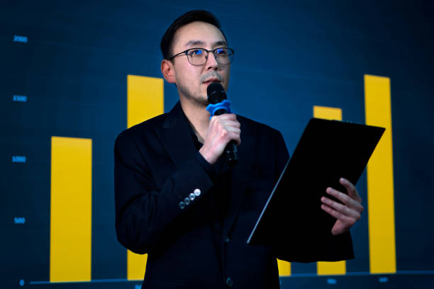 istock Smart businessman in glasses holding microphone on the scene during conference 2188052585