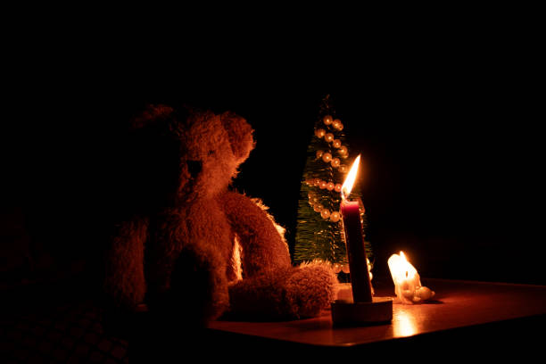 A small New Year tree and a soft children's teddy bear by candlelight in Ukraine without light during the war, New Year without light during the war