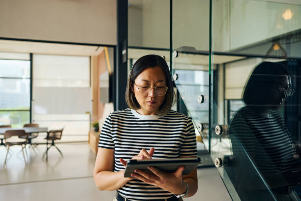 Focused asian businesswoman using digital tablet in modern office, browsing online information