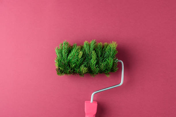Paint roller covered with fir branches on a red background. Conceptual image combining Christmas and creativity, offering a unique take on festive themes.