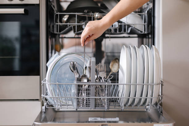 istock Front view from female hand removing clean cutlery from a loaded dishwasher. Background of modern kitchen 2188075597