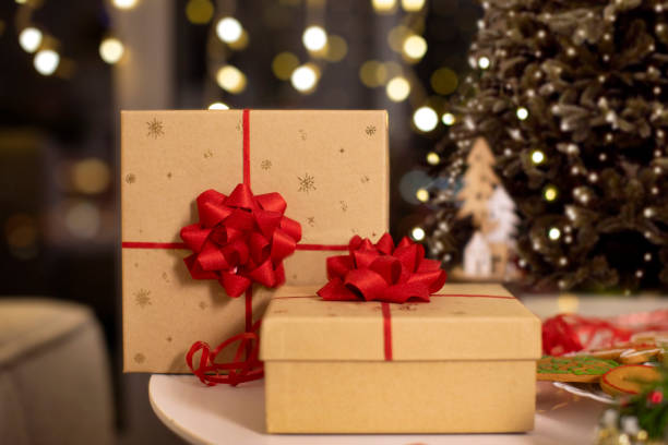 istock Focus on wrapped presents on table and Christmas pine tree with holiday decorations on background. Bokeh lights glowing in the evening 2188076884
