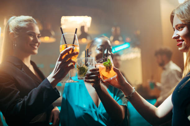 A multiracial group of young female friends enjoying their drinks and toasting on the dance floor.