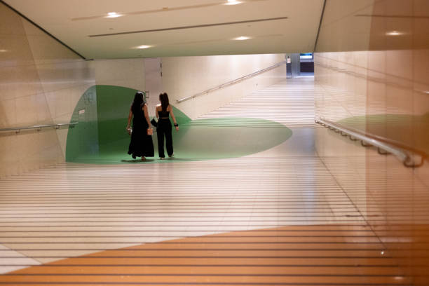 Singapore, Singapore - November 14, 2024: Two women in elegant black outfits walk through a modern underground walkway in Singapore, featuring minimalist design, striped flooring and green accents.\