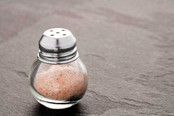 Hand is holding salt shaker with salt on soft black background.