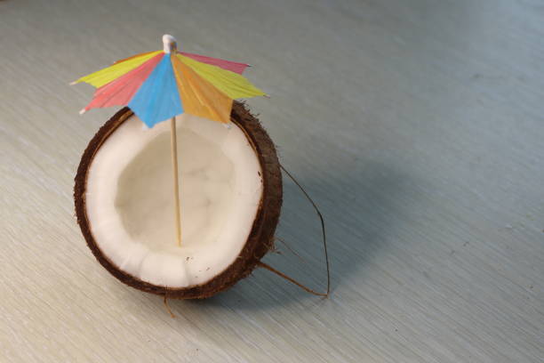 istock Coconut Half Decorated with a Colorful Umbrella Set Against a Light Colored Surface 2188111789